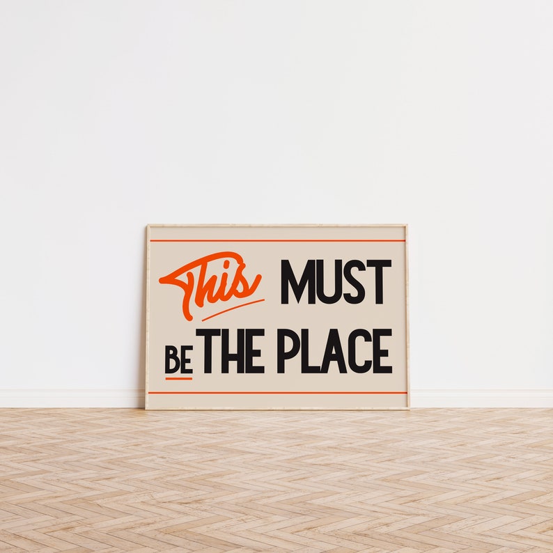 May include: A beige framed poster with the text "This Must Be The Place" in black and orange lettering.
