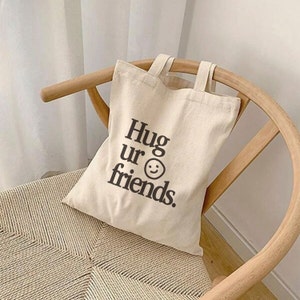 May include: A beige canvas tote bag with black text that reads "Hug ur friends." and a smiley face.