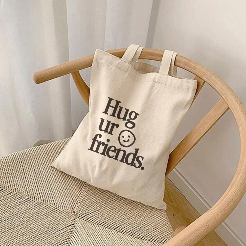 May include: A beige canvas tote bag with black text that reads "Hug ur friends." and a smiley face.