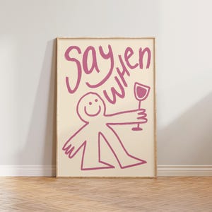May include: A rectangular wall art print featuring a cream background with a dark pink hand-drawn illustration of a smiling stick figure holding a wine glass. The text "Say when" is written in a matching dark pink, loose, handwritten script style.