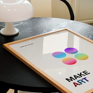 Pode incluir: Um p&ocirc;ster emoldurado com fundo branco e c&iacute;rculos coloridos. O texto "make art, not war" e "MAKE ART" est&atilde;o impressos no p&ocirc;ster.