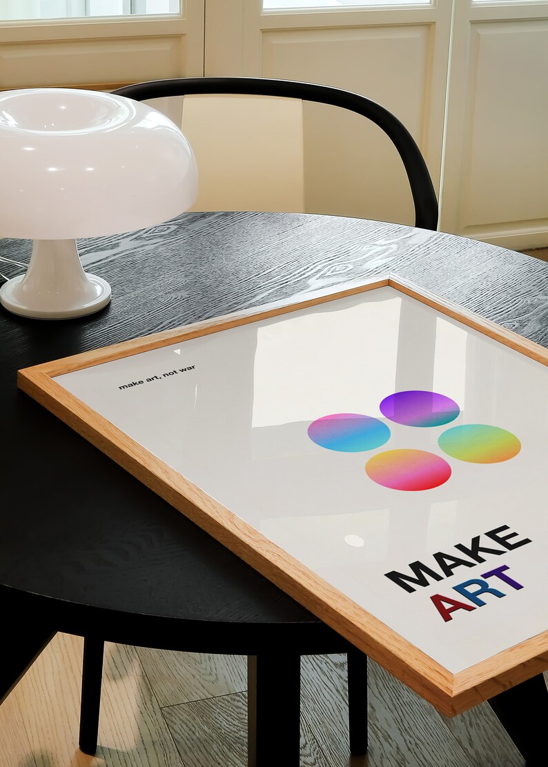 Pode incluir: Um p&ocirc;ster emoldurado com fundo branco e c&iacute;rculos coloridos. O texto "make art, not war" e "MAKE ART" est&atilde;o impressos no p&ocirc;ster.