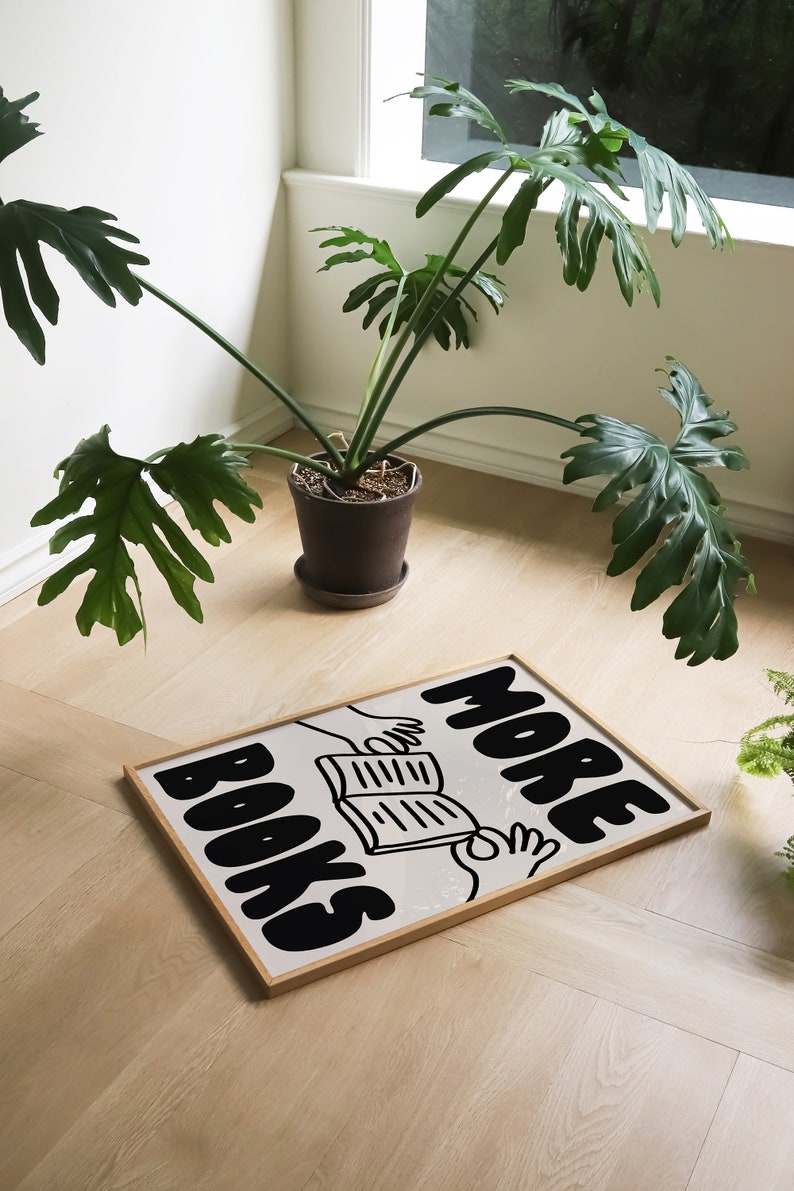 Peut inclure: Une impression encadr&eacute;e avec une illustration en noir et blanc de deux mains tenant un livre ouvert. Le texte "MORE BOOKS" est &eacute;crit en grandes lettres grasses.