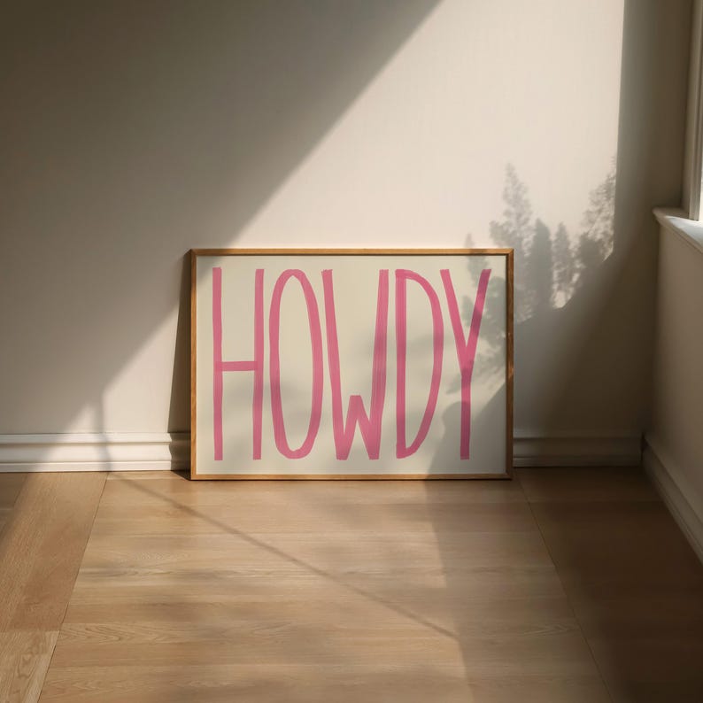 Puede incluir: Una impresi&oacute;n enmarcada con la palabra "HOWDY" escrita en rosa sobre un fondo blanco.