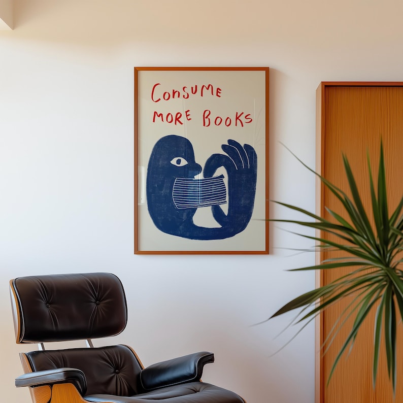 May include: A framed poster with a blue illustration of a person consuming a book. The text on the poster reads "Consume More Books".