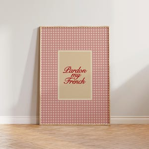 Może przedstawiać: Oprawiony wydruk z r&oacute;żowo-białym wzorem w kratkę gingham. Wydruk przedstawia beżowy prostokąt z napisem "Pardon my French" w czerwonym skrypcie. Rama jest w jasnym kolorze drewna.