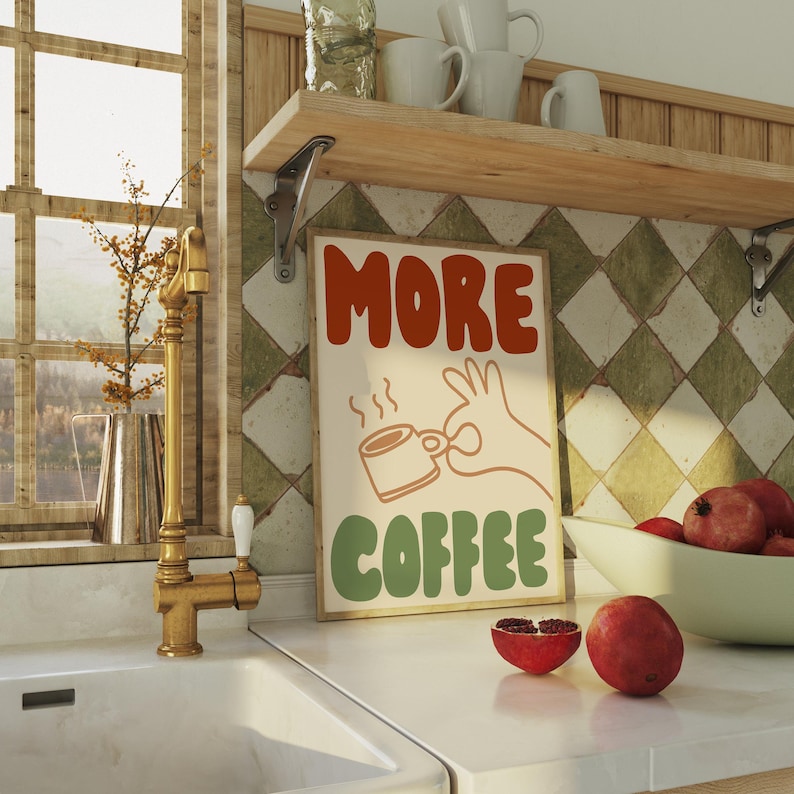 May include: A retro-style poster with the text "MORE COFFEE" in colorful, stylized lettering. A cartoon hand holds a steaming cup of coffee. The poster has a cream background with green and orange accents.