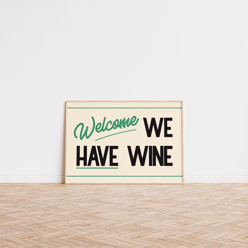 May include: A framed print with a white background and black text that reads "Welcome We Have Wine". The word "Welcome" is written in green cursive.
