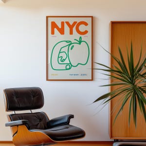 May include: A framed poster with the text "NYC" in orange letters, a green apple with a hand holding it, and the text "The Big Apple That Never Sleeps" in smaller letters below.