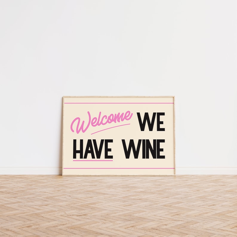 May include: A framed print with a cream background and black text that reads "Welcome We Have Wine". The word "Welcome" is in pink cursive.