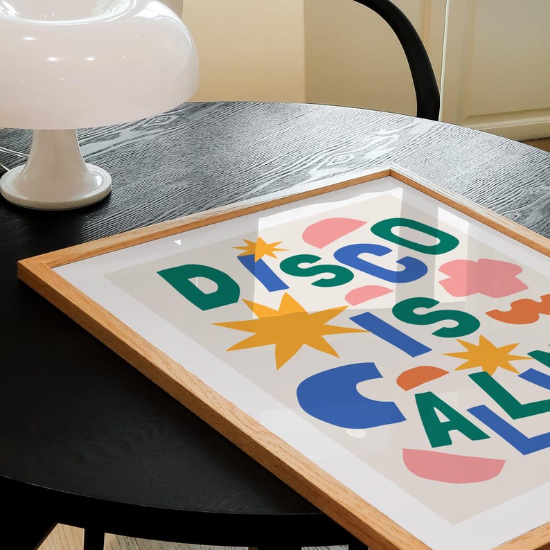 May include: A framed print with the text "Disco is Calling" in colorful, abstract letters. The background is a light beige with pink, blue, and orange shapes.