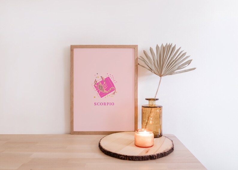 May include: A framed print featuring a light pink background with a central graphic of a scorpion over a bright pink square, surrounded by small gold stars and dots, with the word SCORPIO printed in pink below the illustration.