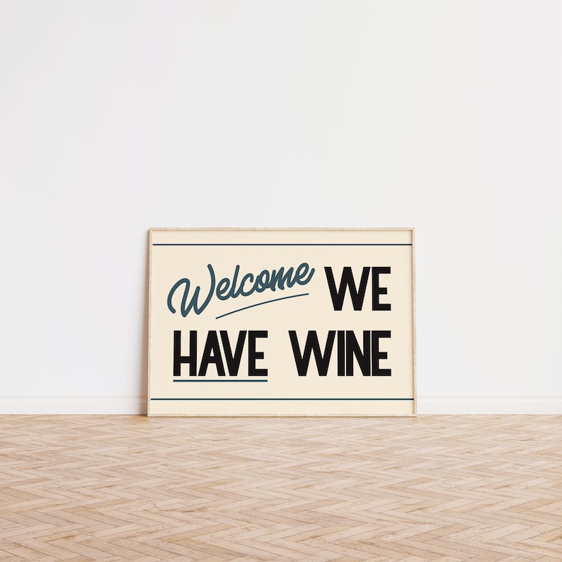 May include: A framed sign with a cream background and a black wooden frame. The sign says "Welcome We Have Wine" in a retro font. The word "Welcome" is in a blue cursive font.