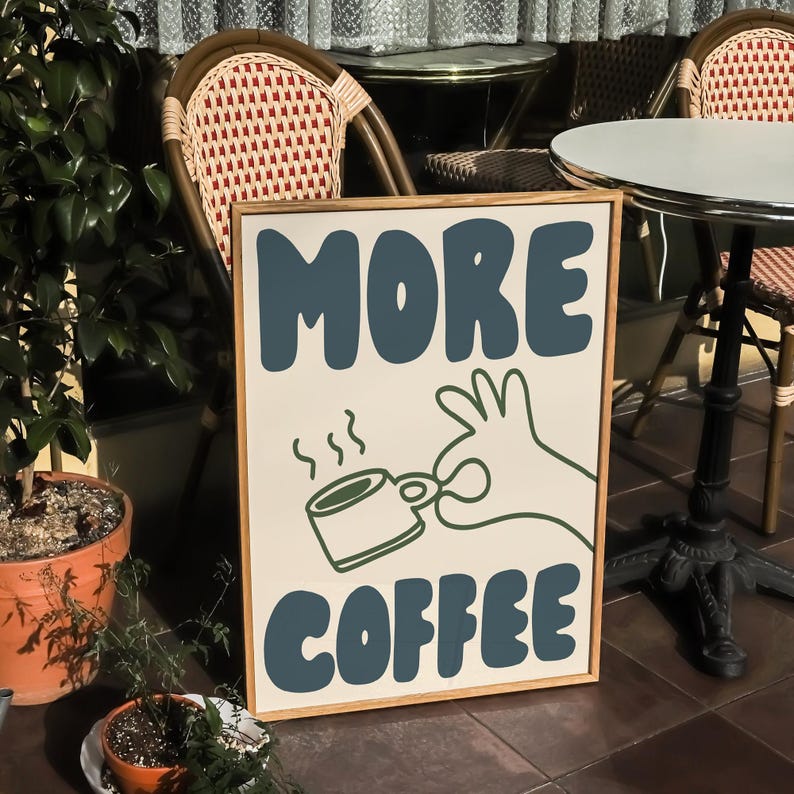 May include: A brown and white sign with the text "MORE COFFEE" in blue letters. A green hand with a cup of coffee is holding a steaming cup of coffee.