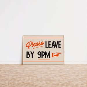 May include: A framed sign with the words "Please LEAVE BY 9PM" in black and orange lettering. The sign has a beige background and a pointing hand graphic. The frame is a light brown color.