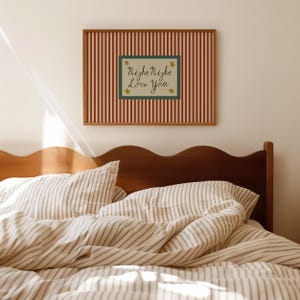 K&ouml;nnte beinhalten: Ein gerahmtes Wandbild mit rot-wei&szlig; gestreiftem Hintergrund und einem gr&uuml;nen Rechteck in der Mitte. Der Text "Night Night Love You" ist in Schreibschrift geschrieben, mit goldenen Sternen. &Uuml;ber einem Bett mit gestreifter Bettw&auml;sche.