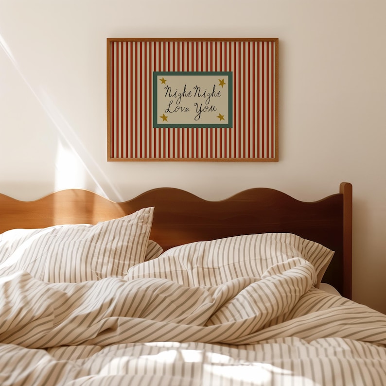 K&ouml;nnte beinhalten: Ein gerahmtes Wandbild mit rot-wei&szlig; gestreiftem Hintergrund und einem gr&uuml;nen Rechteck in der Mitte. Der Text "Night Night Love You" ist in Schreibschrift geschrieben, mit goldenen Sternen. &Uuml;ber einem Bett mit gestreifter Bettw&auml;sche.