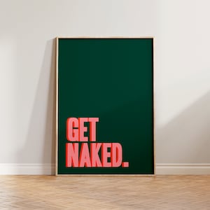 May include: A rectangular wall art print in a light wood frame featuring a dark forest green background with the text GET NAKED in bold, coral-pink, block-style capital letters with a subtle drop shadow effect centered on the print surface.
