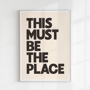 Puede incluir: Una impresi&oacute;n enmarcada con fondo beige y texto negro que dice "This Must Be The Place".