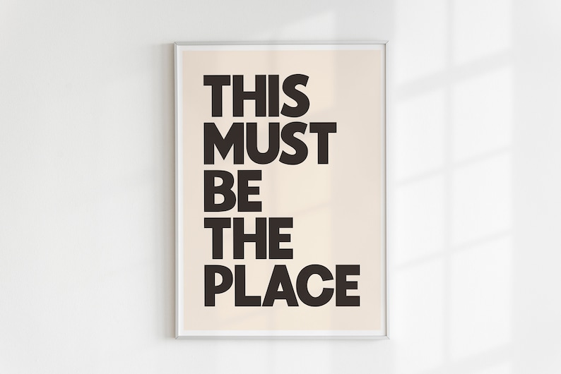 Puede incluir: Una impresi&oacute;n enmarcada con fondo beige y texto negro que dice "This Must Be The Place".