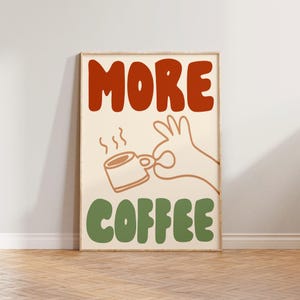 May include: A beige poster with the text "MORE COFFEE" in red and green letters. A cartoon hand holds a steaming cup of coffee.