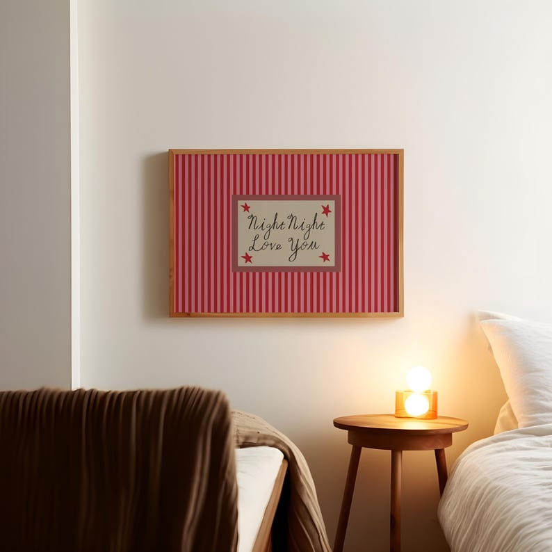 K&ouml;nnte beinhalten: Ein gerahmter Druck mit einem rot-rosa gestreiften Hintergrund. Der Druck zeigt ein zentrales Rechteck mit den Worten "Night Night Love You" und Sternakzenten. Der Rahmen ist hellbraun und der Druck h&auml;ngt an einer wei&szlig;en Wand.