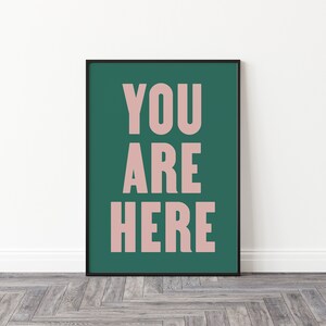 Peut inclure: Une impression encadr&eacute;e avec un fond vert sarcelle et les mots "YOU ARE HERE" en rose clair.