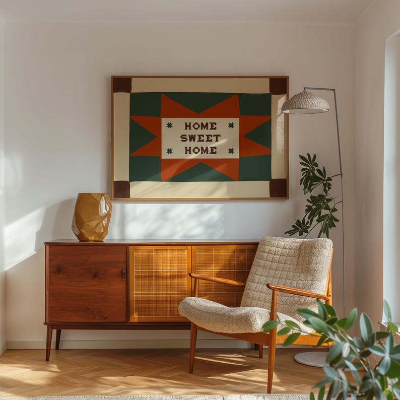Puede incluir: Una impresi&oacute;n de arte mural rectangular en un marco de madera con un patr&oacute;n de estrella geom&eacute;trico en verde oscuro y naranja quemado con el texto HOME SWEET HOME en el centro, flanqueado por cuatro peque&ntilde;as cruces verde oscuro sobre fondo crema.