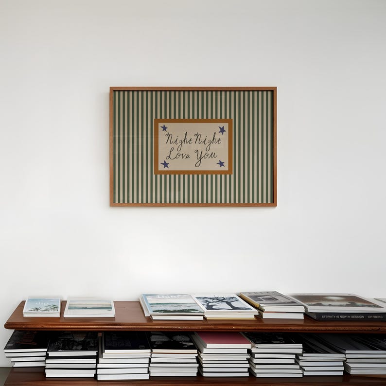 K&ouml;nnte beinhalten: Ein gerahmtes Kunstwerk mit gr&uuml;n-wei&szlig; gestreiftem Hintergrund und einem zentralen Rechteck mit dem Text "Night Night Love You" und blauen Sternakzenten. Das Kunstwerk wird &uuml;ber einem Holzregal mit mehreren B&uuml;chern ausgestellt.