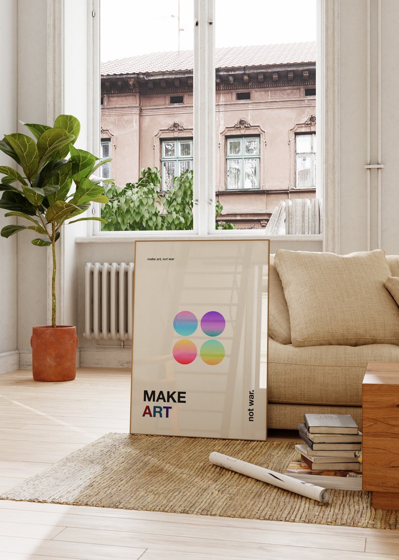 Pode incluir: Um p&ocirc;ster bege com o texto "MAKE ART not war" e quatro c&iacute;rculos coloridos. O p&ocirc;ster est&aacute; pendurado em uma parede de uma sala de estar com um sof&aacute; bege e uma mesa de centro de madeira.