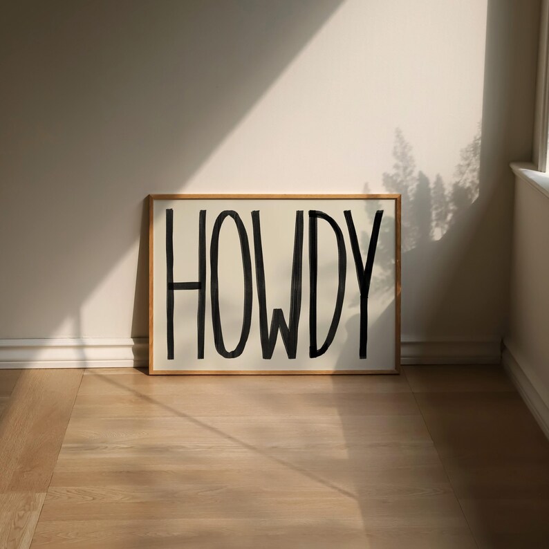 Puede incluir: Una impresi&oacute;n enmarcada con la palabra "HOWDY" escrita en pintura negra sobre un fondo blanco.