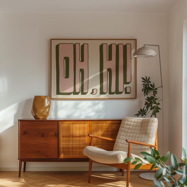 Może przedstawiać: Salon w stylu mid-century modern z brązową drewnianą szafką, białym fotelem i obrazem w ramie z tekstem "Oh Hi!" w r&oacute;żowych i zielonych literach.