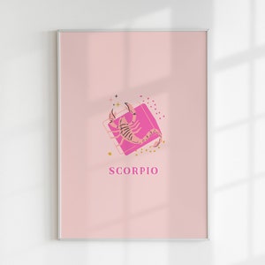 May include: A framed wall art print featuring a light pink background with a central illustration of a scorpion in a darker pink shade. The design includes small gold star and dot accents, a pink square frame, and the word SCORPIO in pink text.