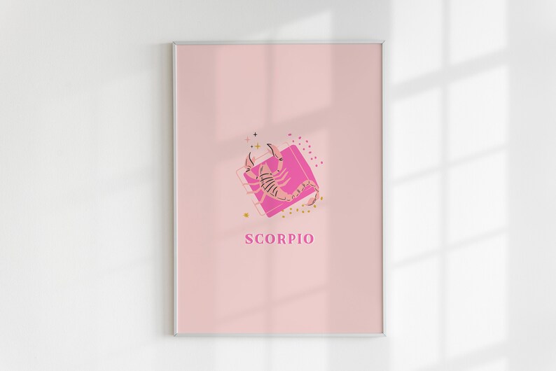 May include: A framed wall art print featuring a light pink background with a central illustration of a scorpion in a darker pink shade. The design includes small gold star and dot accents, a pink square frame, and the word SCORPIO in pink text.