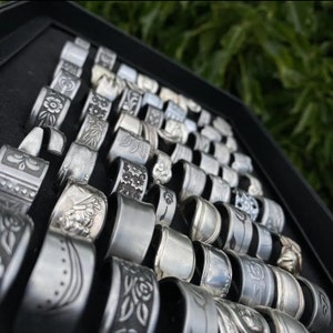 May include: A collection of silver spoon rings displayed in a black velvet box. The rings are made from vintage silverware and feature various engraved designs.
