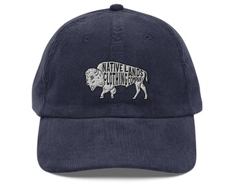 May include: Navy blue corduroy baseball cap featuring the text "NATIVE LANDS CLOTHING COMPANY" in white, with a white bison graphic. The cap has a curved brim and a rounded crown. A classic, casual accessory.