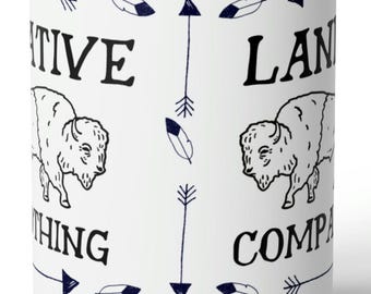 May include: A white ceramic mug featuring a black line drawing of a bison, dark blue arrows, and feathers. The text reads NATIVE LAND COMPANY. The design is repeated around the mug with vertical arrows separating the bison illustrations.