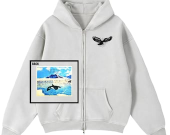 May include: A light gray zip-up hoodie featuring a black eagle graphic on the upper right chest. An inset box labeled BACK displays a graphic of an orca swimming in icy blue waters with mountains and the text NATIVE LANDS CLOTHING COMPANY.