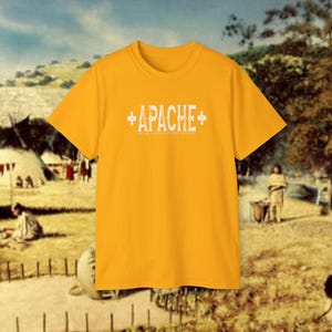 May include: A yellow t-shirt with a white graphic print that says "APACHE" with plus signs on either side. The text below says "NATIVE AMERICAN CLOTHING COMPANY."