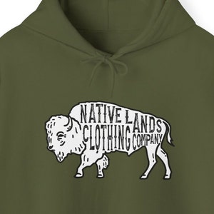 Może przedstawiać: Zielona bluza z kapturem z białym nadrukiem przedstawiającym bizony z napisem "NATIVE LANDS CLOTHING COMPANY".