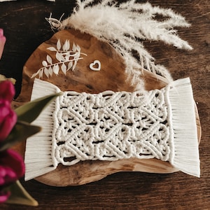 Könnte beinhalten: Weißer Makramee-Untersetzer mit Fransen auf einer Holzoberfläche. Der Untersetzer hat ein geometrisches Muster und ist aus Naturfasern gefertigt.