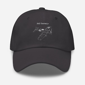 Könnte beinhalten: Dunkelgraue Baseballkappe mit einer weißen Strichzeichnung eines F4U Corsair Flugzeugs. Der Text "F4U Corsair" befindet sich über der Flugzeuggrafik. Die Kappe hat einen gebogenen Schirm und einen Stoffverschluss.