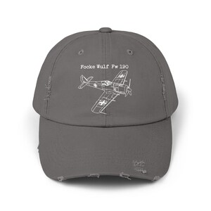 Peut inclure: Casquette de baseball grise délavée avec un dessin au trait blanc d'un avion Focke Wulf Fw 190. Le texte "Focke Wulf Fw 190" est au-dessus de l'illustration de l'avion. La casquette a un aspect vieilli.