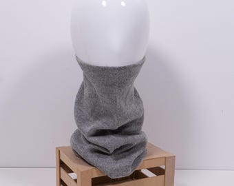 May include: A gray knit cowl neck warmer displayed on a white mannequin head. The neck warmer is made of a soft, textured material and is draped over a small wooden crate. The cowl is a solid gray color.