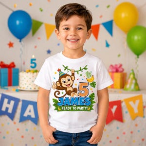 May include: A white short-sleeved t-shirt featuring a cartoon monkey wearing a party hat, hanging from a vine. The graphic includes the number 5, the name JAMES, and the text READY TO PARTY, surrounded by tropical leaves and bananas.