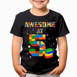 May include: Black t-shirt with the text "AWESOME AT 5" in colourful letters. The number 5 is made of colourful toy building blocks.