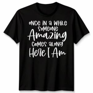 May include: Black t-shirt with white text. The text reads "ONCE IN A WHILE SOMEONE AMAZING COMES ALONG HERE I AM" in a mix of fonts. The shirt has short sleeves and a crew neck.