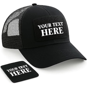 May include: Black trucker cap with a mesh back and a curved peak. The cap has a rectangular patch with the text "YOUR TEXT HERE" in white. A matching black square coaster with the same text is also present.
