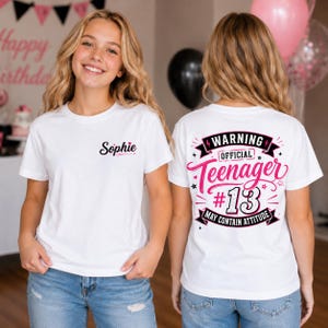 May include: A white short-sleeve t-shirt featuring the name Sophie in black script on the front left chest. The back displays a graphic with the text WARNING OFFICIAL Teenager #13 MAY CONTAIN ATTITUDE in black and pink with star accents.