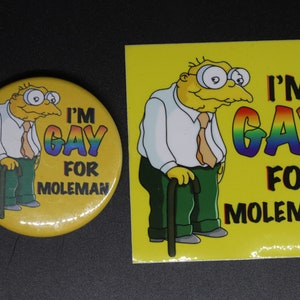 May include: A yellow button with a cartoon image of a man with a cane and the text "I'm Gay for Moleman" in rainbow letters.